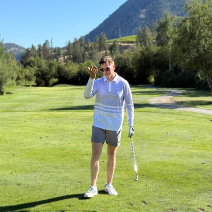 Man on a golf course with mountains and trees in the background wearing a lavender colored UPF 50+ long sleeve golf polo